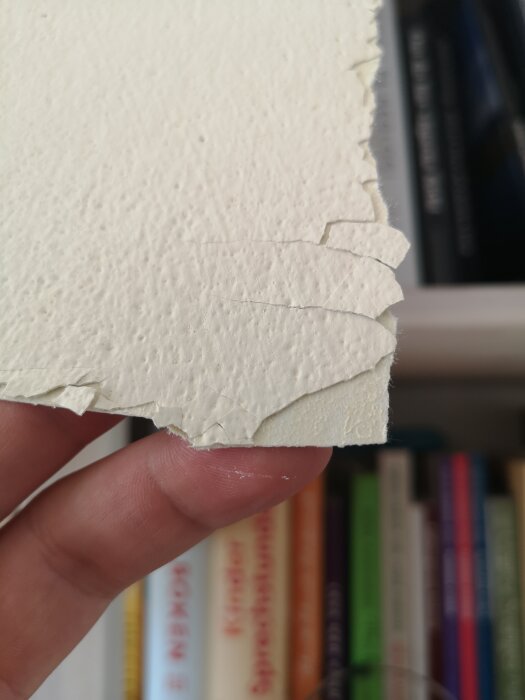 Hand håller kantstansat, handgjort papper med böcker i oskarp bakgrund.