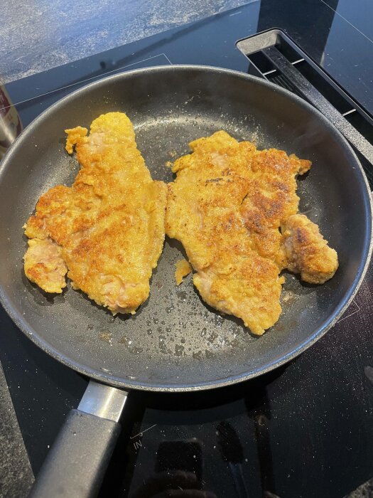 Två pannstekta schnitzlar på en stekpanna på spishäll, gyllenbruna, tillagade i köket.