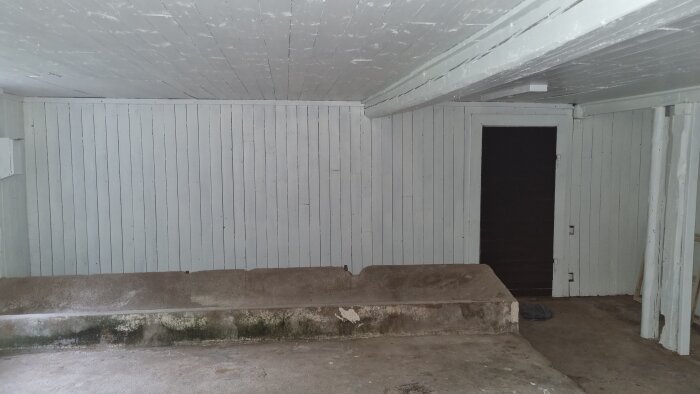 Ett tomt rum med vita väggar och tak, en betongsockel, och öppen dörr.