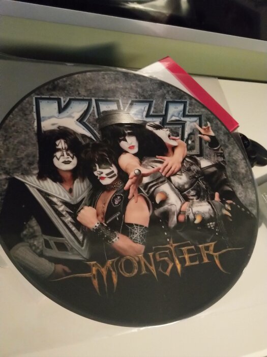 Rund vinylskiva med KISS i full smink och kostym, albumtitel "Monster" nedanför bandmedlemmarna.