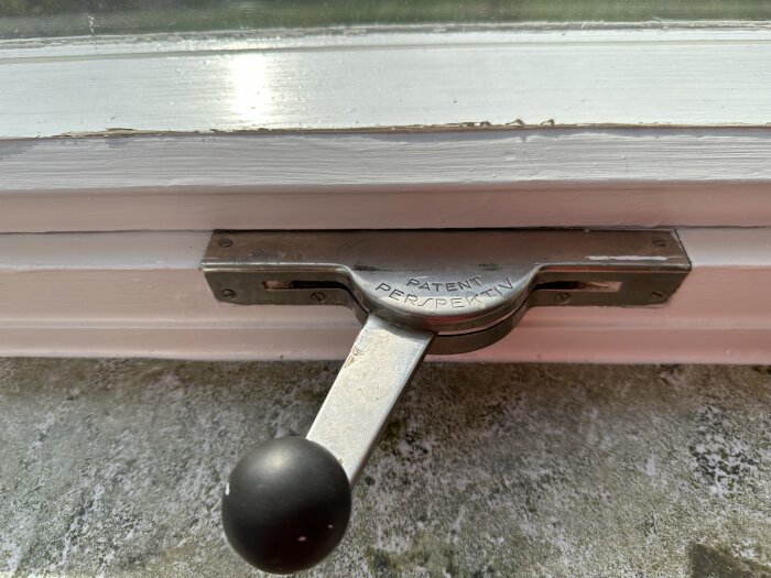 Fönsterhandtag i metall på ett vitt fönster, märkt "PATENT ESPERPEX-TV", smutsig fönsterbleck.