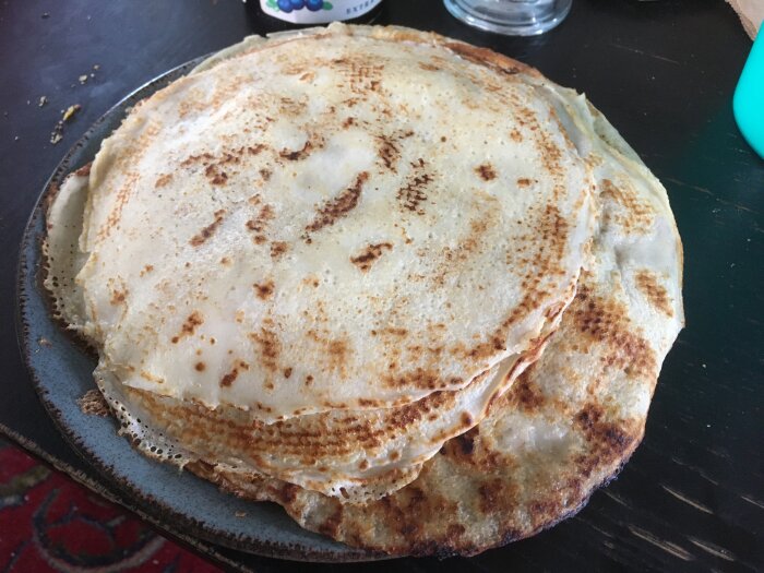 En hög med gyllenbruna pannkakor på blå tallrik, köksbord i bakgrunden, hemgjord frukost eller brunch.
