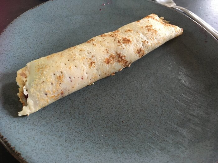 En tunn, stekt pannkaka med fyllning, serverad på en mörkblå tallrik.