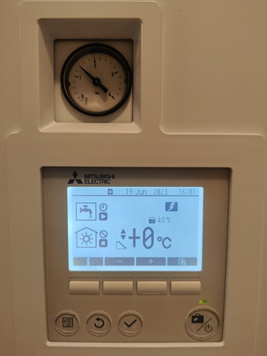 Värmepumpens kontrollpanel med klocka, display och knappar visar datum, tid och temperaturinformation.