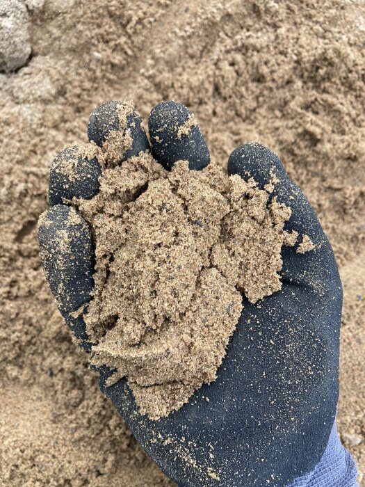 En hand täckt av sand och en sandslottsbyggande handske, närbild, skapar lekfull textur.