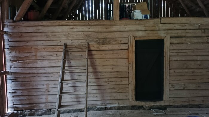 Ett gammalt vedskjul med stegar, öppen dörr och saker på loftet.