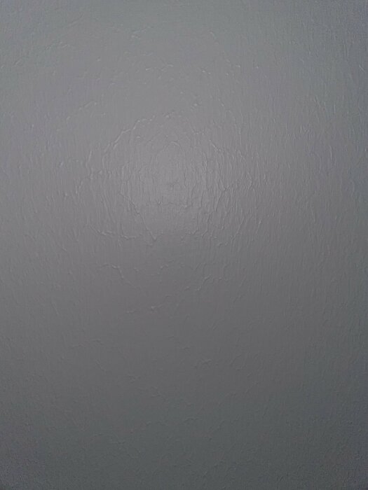 En grå vägg med en cirkulär textur av spackel eller målararbete, som skapar subtil variation i ytan.
