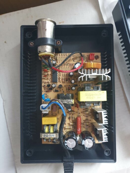 Elektronikkort inuti svart hölje med komponenter, kondensatorer, kopplingar, och anslutningar.