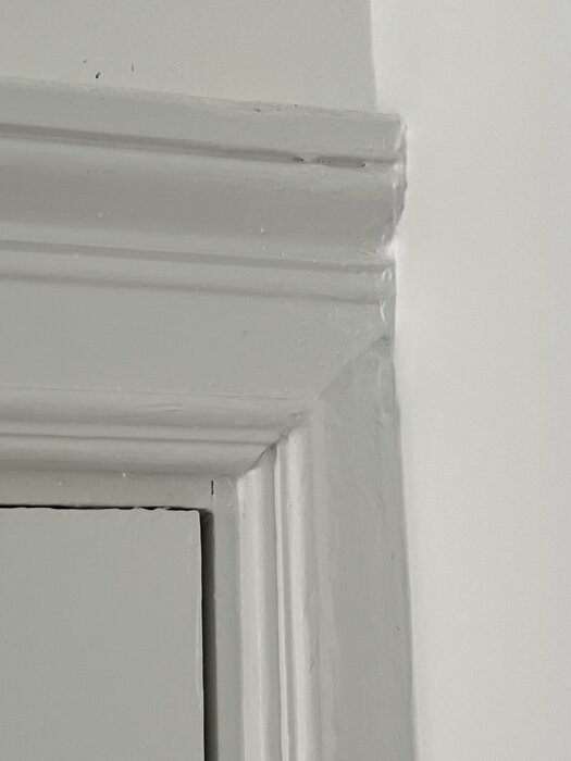 Hörnet av en vitmålad dörrkarm och vägg, detaljer av listverk synligt.