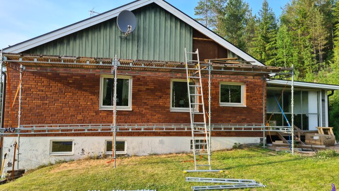 Ett hus med tegelfasad och ställningar indikerar pågående renovering eller underhåll. Satellitantenn och träd synliga.