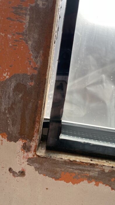 Bilden visar fönsterhörn med sliten färg och rost, behöver underhåll och reparation.