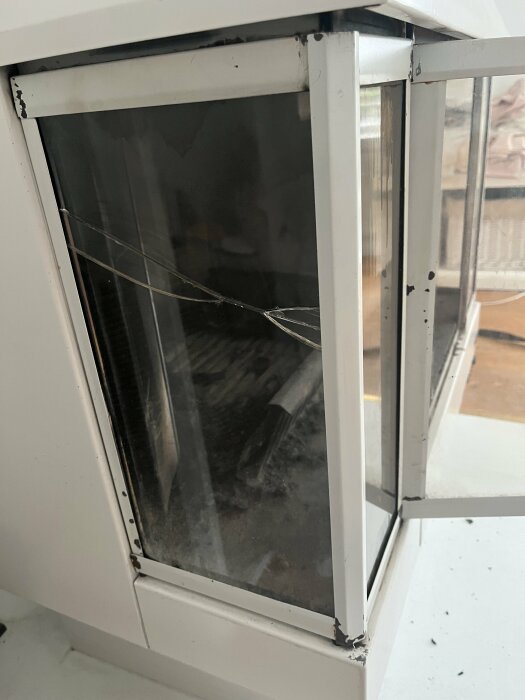 Sprucket fönsterglas i vit karm, smutsigt, med synliga dammpartiklar och en spegling.