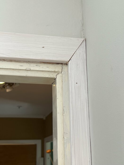 Vit dörrkarm med sprickor, slitage och behöver eventuellt reparation eller ommålning, i ett inomhusutrymme.