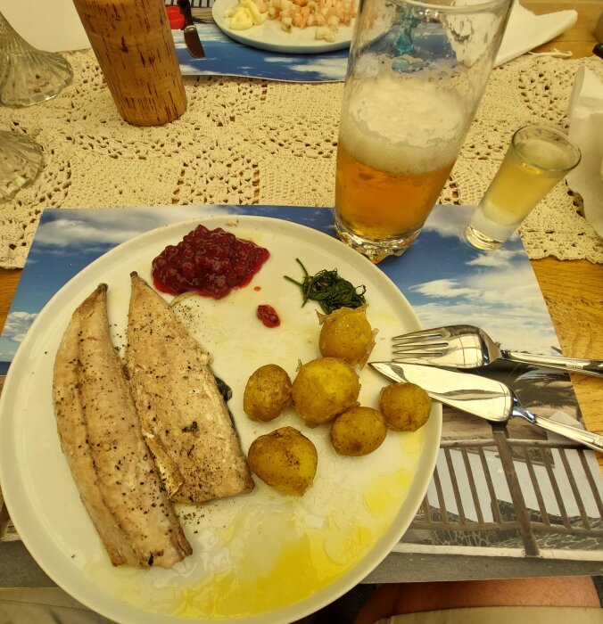 En måltid med fisk, potatis, lingonsylt, spenat samt öl och snaps i sommarmiljö.