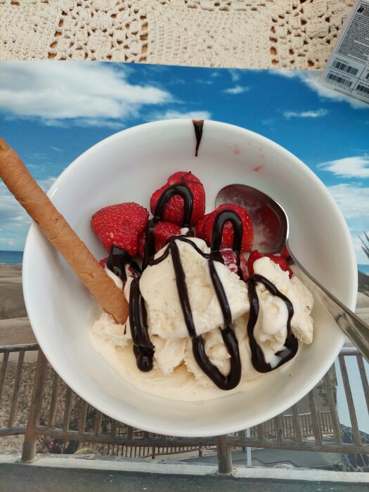 Glass med jordgubbar och chokladsås, kex, mot bakgrund av strand och himmel.