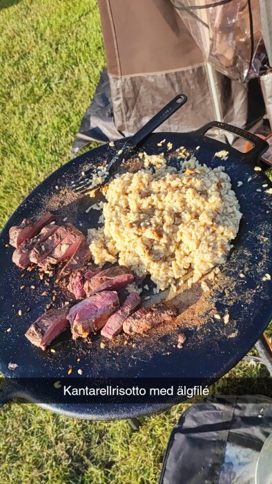 Stekpanna med kantarellrisotto och älgfilé, utomhus grön gräsmatta, campingstol i bakgrunden.