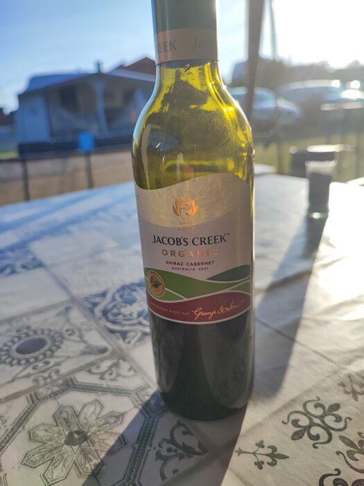 Flaska Jacob's Creek Organic Shiraz Cabernet vin på ett bord utomhus med solen i bakgrunden.