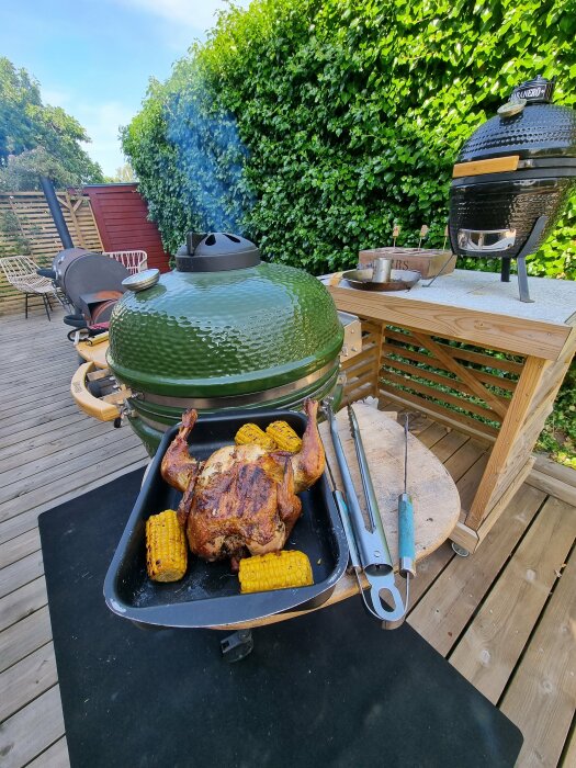 Grillad kyckling och majs på en uteplats med en Big Green Egg-grill och rök som stiger.
