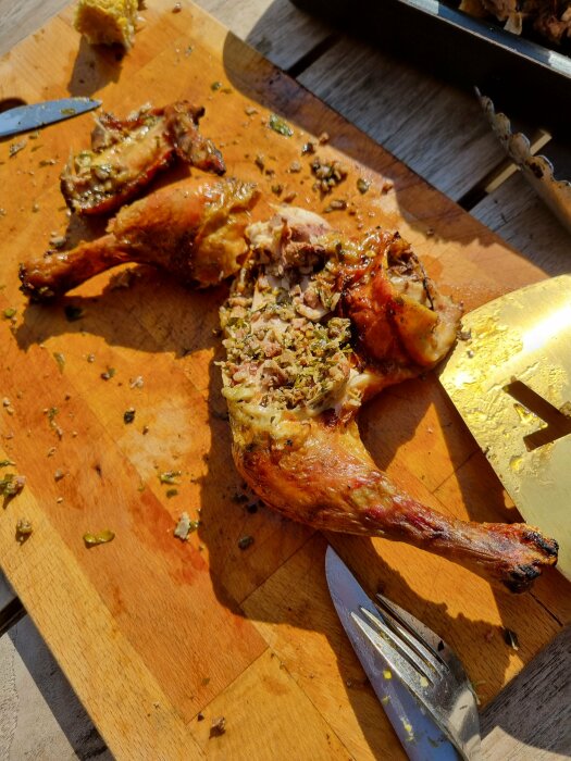 Ugnsstekt kyckling på skärbräda med kryddor, kniv och gaffel. Matlagning, måltid, kök.