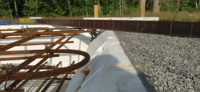 Byggarbetsplats med armeringsjärn, konstruktion i förberedelse, vit isolering och makadamgrund i soligt väder.