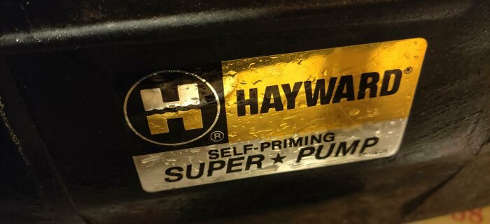 En etikett på utrustning märkt "HAYWARD" och "SELF-PRIMING SUPER PUMP", våt och reflekterande yta.