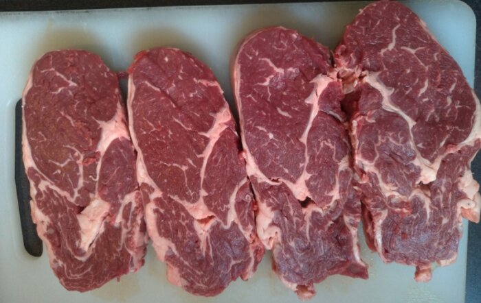 Bitar av rått biffkött, marmorerade med fett, ligger på skärbräda.