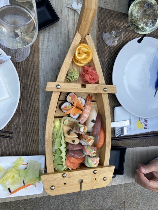 Sushibricka i trä, ingefära, wasabi, citrus, sallad, vit vintallrik, person vid bordet.