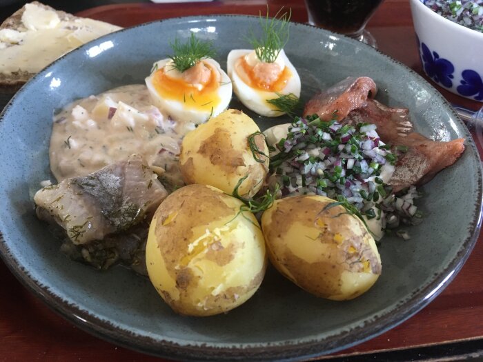Ett fat med svensk mat: sill, kokt potatis, ägg, dillsenapssås, rödlök och knäckebröd med ost.