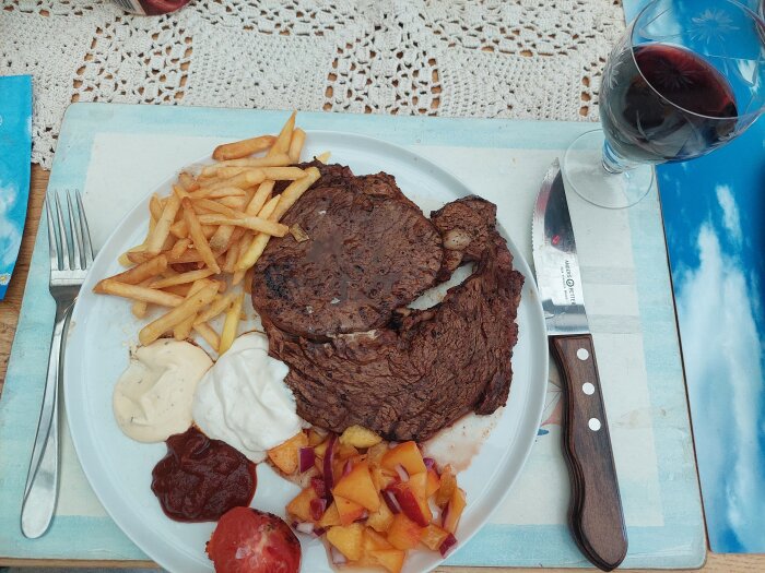Stekt biff, pommes, såser, sallad, rött vin, uppdukning på bordet med duken.