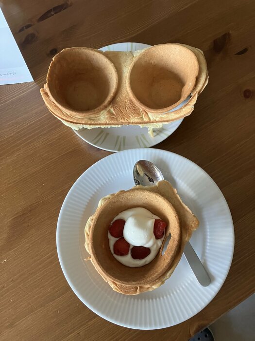 Pannkakor formade som skålar med grädde och jordgubbar på ett bord.