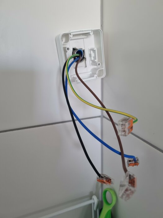 Öppen eluttagsinstallation med exponerade färgade kablar och anslutningsklemmar på en vit vägg.
