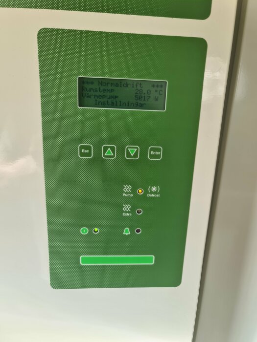 Grönt kontrollpanel för värmepump med LCD-skärm som visar temperatur och effekt samt knappar för navigering.