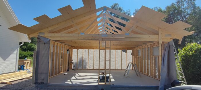 Träkonstruktion av en byggnad under uppförande, takstolar synliga, soligt väder.