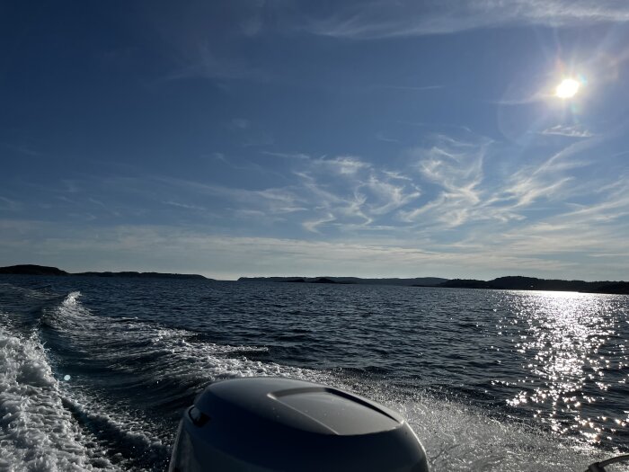 Motorbåt på soligt hav, vågor och skum, öar i bakgrunden, blå himmel.