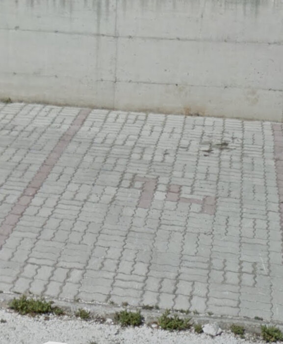 Gatsten med mönster nära en betongvägg och lite gräs vid kanten.