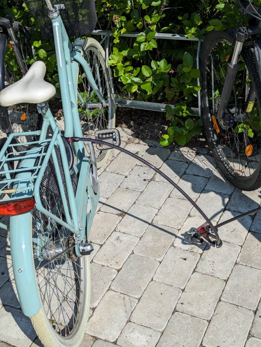 Två cyklar parkerade, en i turkos och en svart, med en låskedja fast i stolpe.