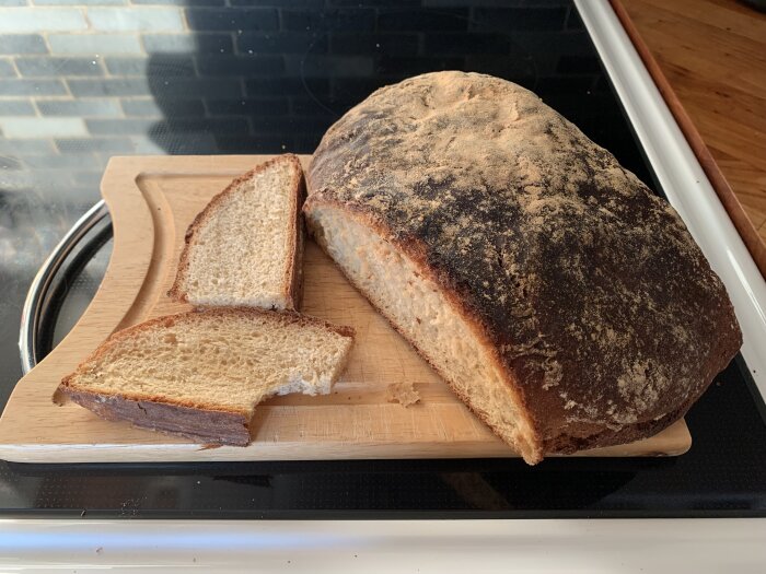 Hembakat bröd på skärbräda, två skivor avskurna, köksbänk bakgrund.