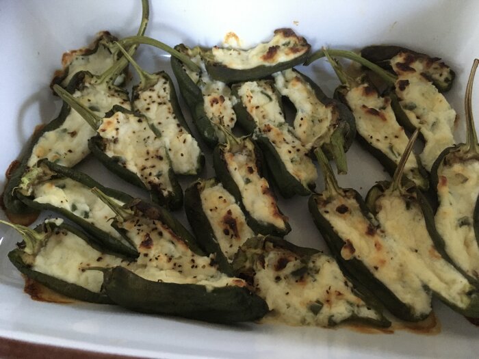 Grillade jalapeños fyllda med ost, gräddade till de fått färg, serverade i en vit behållare.