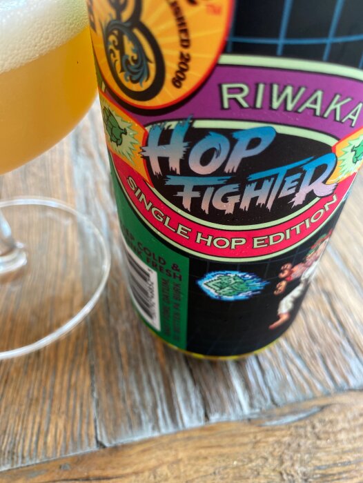 Ölflaska med etikett "Hop Fighter", glas med ölskum, träbord, delvis suddig förgrund, fokus på etikett.