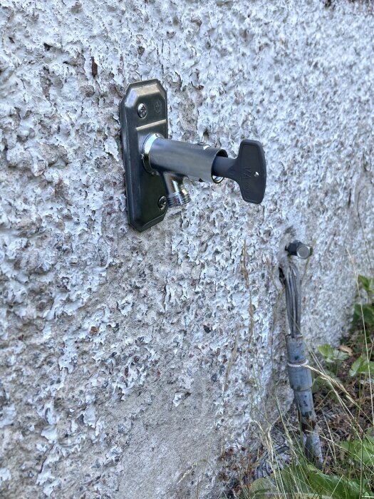 Låscylinder med nyckel i betongvägg, bredvid gammal, rostig vattenkran.