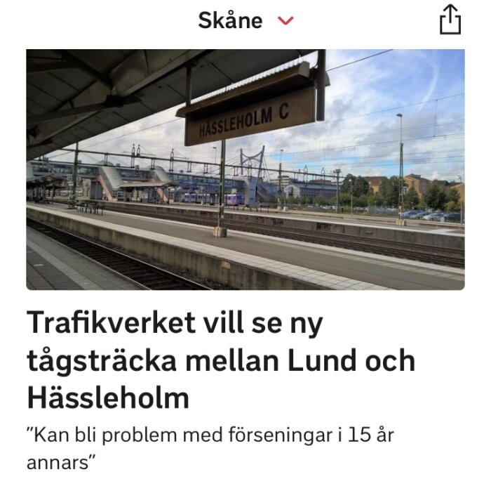 Tågstation, skylt "Hässleholm C", artikel om ny tågsträcka, potentiella förseningar nämnda.