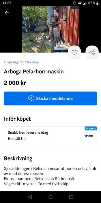 Stående pelarborrmaskin till salu, placerad utomhus vid röd vägg, skuggor, grönska i bakgrunden.