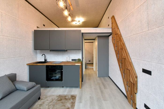 Modernt kök med grå skåp, trätrappa, grå soffa, ljusa väggar och unik taklampa.