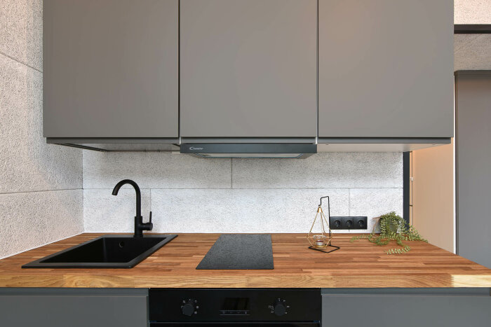 Modernt kök, grå skåp, träbänkskiva, svart diskho och kran, inbyggd ugn, minimalistisk design.