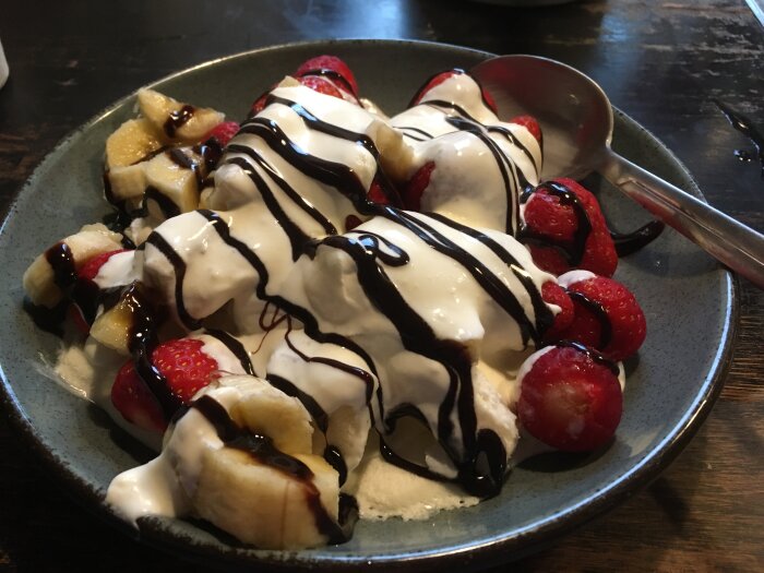 Bananskivor, jordgubbar, glass, chokladsås, efterrättsskål, sked, grått fat.