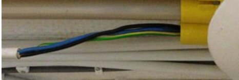 Elkabel med blå, brun, och grön/gul ledare exponerad i en vit kabelkanal. Installationsmiljö, potentiell säkerhetsrisk.