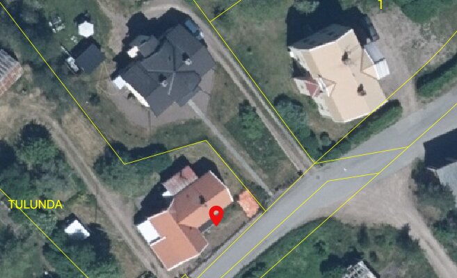 Satellitbild av bostadsområde med hus, vägar och grönska, markerat platsintresse med röd symbol.