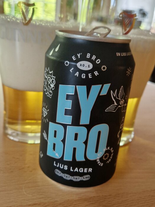 Ölburk framför delvis synligt ölglas. "EY BRO" märkning, mörk design, "Ljus Lager", grafiska detaljer.