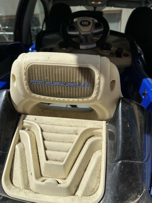 Bild av en dammig barnbil interiör med ratt och märkesnamn synligt.
