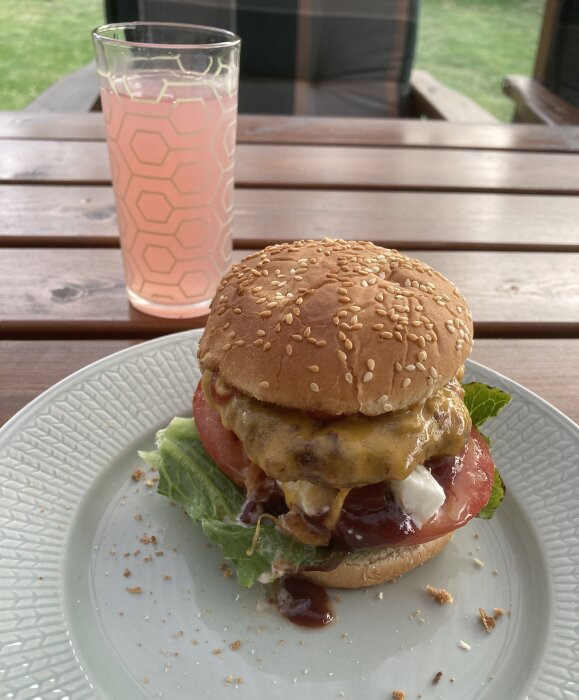 Cheeseburgare på tallrik med rosa dryck i hexagonmönstrat glas, utomhus på träbord.